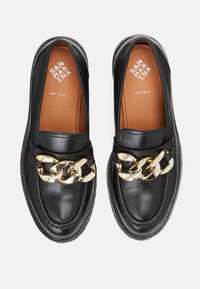 Paire de mocassins en cuir noir avec un détail de chaîne dorée épaisse et des semelles intérieures beige marquées "San Marina Vera Pelle" sur un fond blanc.