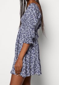 Vestido con estampado floral en tonos azules, de manga corta, con cuerpo fruncido y falda acampanada, hecho de tela ligera.