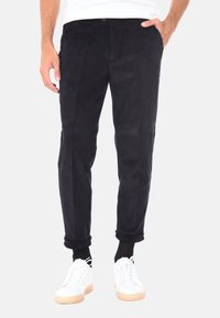 Pantaloni in velluto a coste neri con taglio dritto, caratterizzati da righe verticali e orli arrotolati, abbinati a sneaker bianche per un look casual.