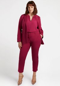 Costum fuchsia cu sacou croit, bluză plisată și pantaloni slim-fit. Textură clară, siluetă ascuțită și tocuri elegante completează look-ul.