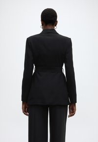 Μαύρο σακάκι κολλητό με εφαρμοστή μέση, μακριά μανίκια και μία μονή χαραγή στο πίσω μέρος. Διαθέτει λεία υφή και μινιμαλιστικό σχέδιο.