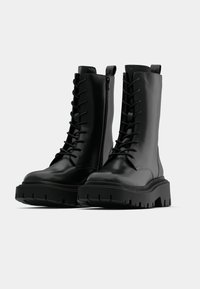 Black leather lace-up boots with a chunky rubber sole, featuring a side zipper and distinctive textured finish.