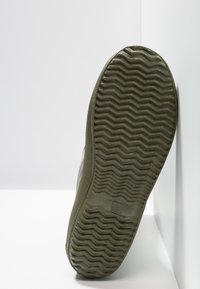 Olijfgroene schoenzool met een golvend profiel en textuurranden. Bevat een nummerafdruk en eenvoudig, functioneel ontwerp.
