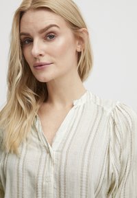 Blusa de cuello en crema claro con rayas verticales, tejido texturizado y sutil abertura de botones. Con caída suave y mangas abullonadas.