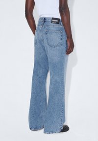 Jeans de mezclilla de campana en azul claro con una cintura de altura media, que presentan dos bolsillos traseros y una etiqueta negra en la cinturilla. Tejido texturizado.