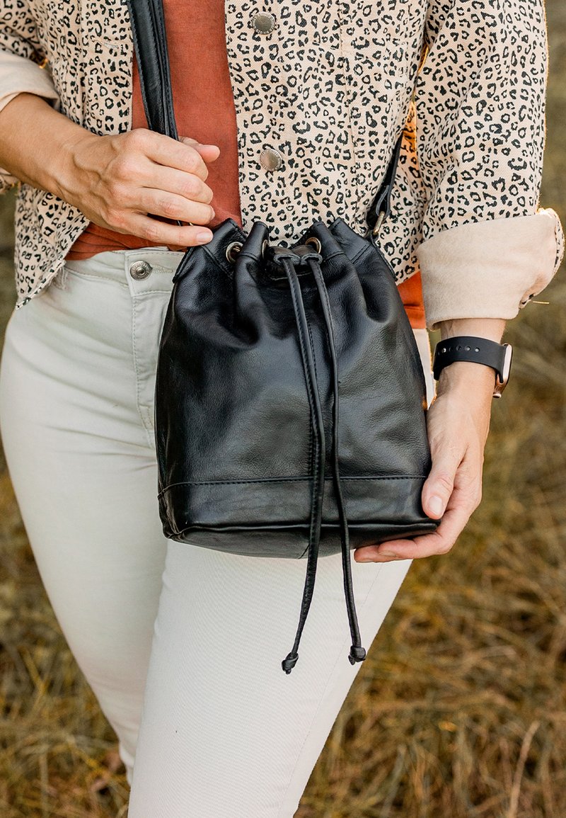 Borsa a secchiello nera in pelle con chiusura a coulisse, texture liscia e base a contrasto. Accessoriata con una sottile tracolla.