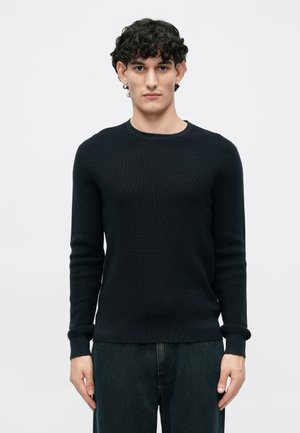 Pull en maille bleu marine avec un motif texturé, col rond et manches longues. Associé à un pantalon en denim foncé pour un look décontracté.