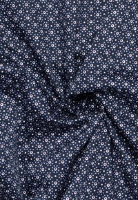 Tessuto di cotone con uno sfondo navy e un motivo geometrico ripetitivo in bianco e bordeaux, con piccoli motivi floreali e forme di diamante.