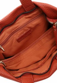 Borsa tote rossa in pelle con esterno testurizzato, aperta per rivelare un interno in tessuto arancione liscio, dotata di molteplici tasche con zip e tasche aperte.