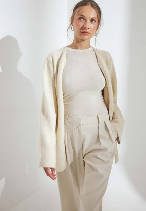 Beige, gebreide cardigan met een open voorkant, lange mouwen en een relaxte pasvorm, gedragen over een aansluitend, lichtbeige top en geplooide, high-waisted broek.