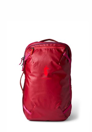 Bright red Cotopaxi Allpa 28 travel backpack with zippered front pocket and carry handle on white background.