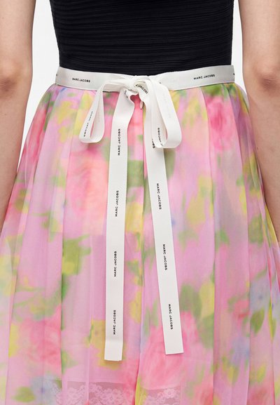 Personne portant un haut noir et une jupe à fleurs pastel, cintrée à la taille avec un ruban blanc Marc Jacobs noué en nœud.