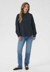 Marineblauwe overhemd met kraag, lange mouwen en een ontspannen pasvorm, gecombineerd met lichtblauwe straight-leg jeans en zwarte ballerina's.