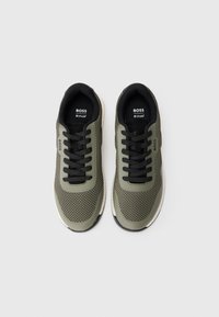 Gröna mesh-sneakers med svarta accenter, med svarta snören, vadderad krage och en vit sula. Varumärkeslogotypen är tydligt synlig.
