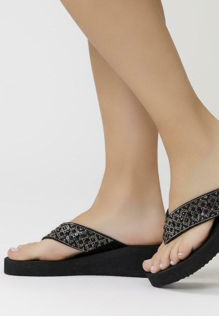 Tongs noires avec des brides texturées ornées de perles en argent, dotées d'une semelle épaisse et d'un design en wedge surélevé.