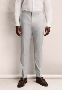 Pantaloni su misura grigio chiaro con una vestibilità slim, dotati di una fascia piatta, passanti per cintura e una texture liscia, abbinati a scarpe in pelle marrone.