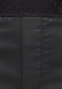 Tejido negro con una textura suave y brillo, que presenta un patrón tejido en el borde superior. Incluye costuras planas y líneas nítidas.