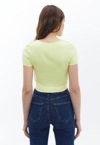 Kortærmet, cropped top i lys gul bomuld, med rund halsudskæring og en glat tekstur, parret med højtaljede blå jeans.