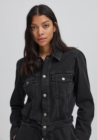 Melissa melnā denima kombinezons ar apkakli, garām piedurknēm, diviem krūšu kabatām un metāla pogām. Izturīga josta ar savāktu tekstūru.