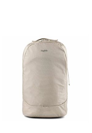 Zaino rettangolare beige con angoli arrotondati, manico superiore, chiusura con cerniera e nome del marchio "Haglöfs" al centro anteriore.