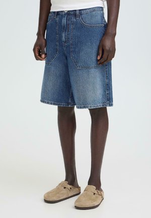 Denimshorts i mellemvaske med en løs pasform, der har to forlommer og et lige snit. Båret med lyse beige slip-on sko.