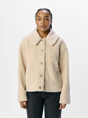 Giacca in fleece beige con ampio colletto, chiusura frontale a bottoni e tasche laterali. Presenta un materiale testurizzato e morbido con una vestibilità leggermente accorciata.