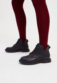 Cizme negre din piele la glezna, cu o finisare netedă, design cu șireturi și talpă din cauciuc. Prezintă vârf rotund și decupaj la gleznă pentru stil.