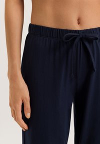 Detailní záběr na osobu v námořnického modrým kalhotách s elastickým pasem a zavázanou šňůrkou, odkrytou střední částí břicha a levou rukou volně položenou na boku.