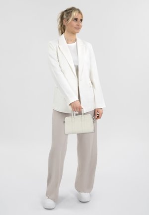 Blazer blanco ajustado sobre una blusa gris claro, combinado con pantalones beige y zapatillas blancas; sosteniendo un pequeño bolso blanco.