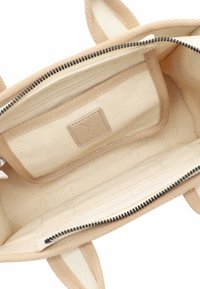 Interno di una borsa tote in tela beige con scomparto con cerniera, fodera di colore chiaro e una piccola etichetta cucita. Texture liscia.