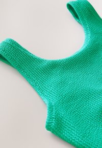 Débardeur vert tricoté avec larges bretelles, doté d'un tissu texturé et d'un col arrondi.