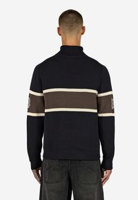 Schwarzer Strickpullover mit hohem Kragen und braunen sowie cremefarbenen Streifen über den Rücken. Verfügt über eine bestickte Verzierung am Ärmel.