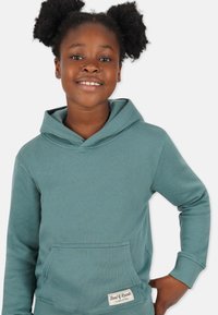 Huoodattu collegepaita teal-värissä, jossa on etutasku, ribbireunat hihansuissa ja helmassa. Pehmeä texture ja klassinen muotoilu. Brändilogo helmassa.
