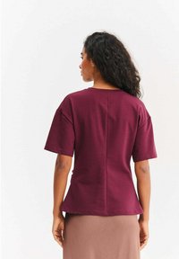 Bordowa bluzka z krótkim rękawem o luźnym kroju, z baskinką i szwem z tyłu. Miękka tkanina o gładkiej fakturze.