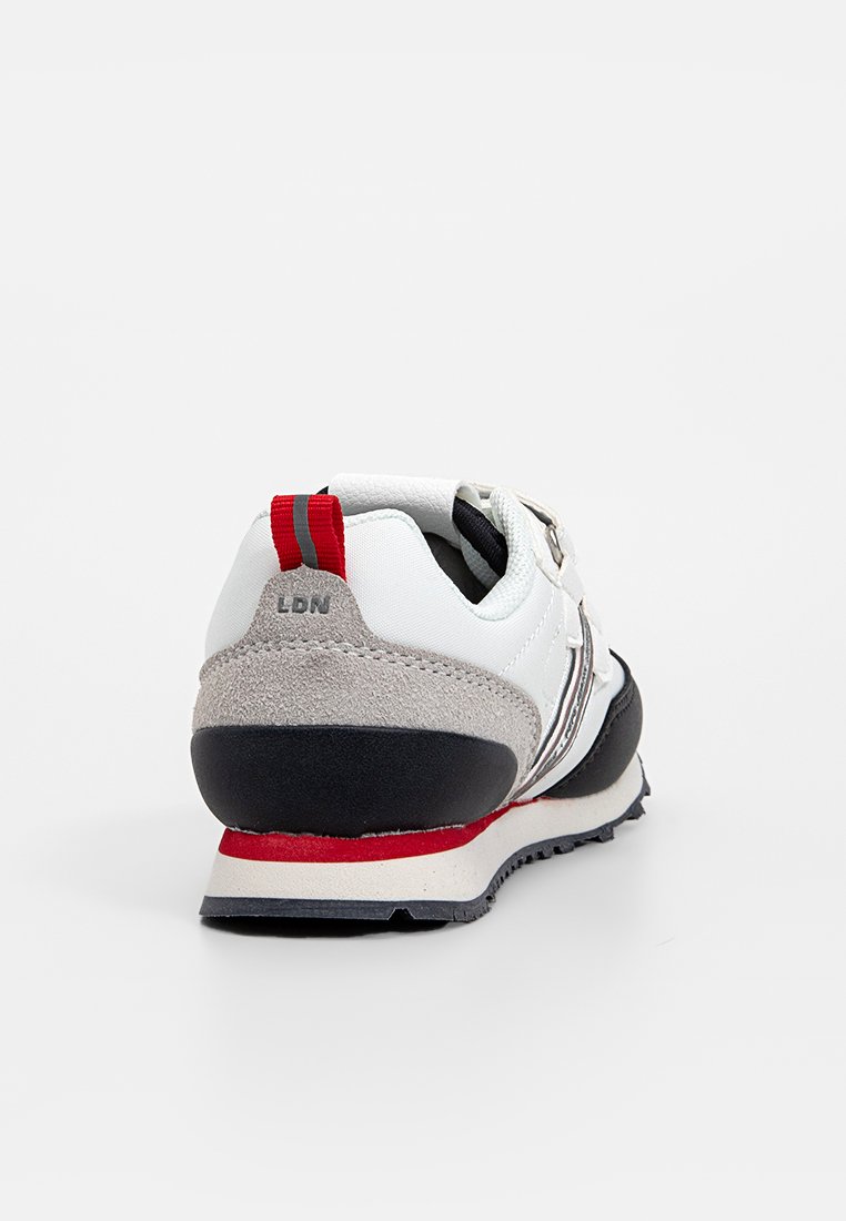 Laufschuh mit einem Obermaterial aus weißem Leder, grauen Wildlederakzenten, einer schwarzen Sohle und einem roten Fersenanhänger. Verfügt über reflektierende Streifen an der Seite.