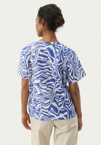 Chemise à manches courtes ample en bleu et blanc avec un motif zèbre. Fabriquée en tissu léger, elle présente un col rond et un design décontracté.