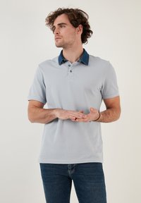 Světle šedé polo tričko s tmavě modrým límcem, krátkým rukávem a zapínáním na tři knoflíky, nošené s tmavě modrými džíny.