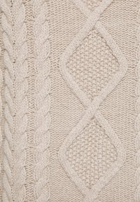 Tejido de punto beige con patrones de cable y diamante, que presenta puntos texturizados y detalles de hilo tejido.