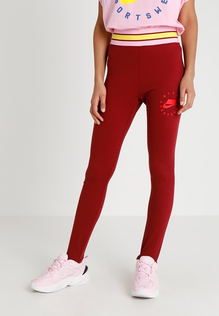 Červené legíny s přiléhavým střihem, s žluto-bílým pruhovaným pasem a malým logem Nike na dolní části nohavice.