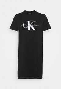 Czarna bawełniana sukienka koszulkowa z krótkimi rękawami i okrągłym dekoltem. Na przedzie wyraźne białe logo Calvin Klein Jeans oraz stylizowana grafika „CK”.