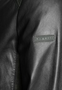 Schwarze Lederjacke mit glatter Textur. Verfügt über ein rechteckiges Bugatti-Logopatch am Ärmel. Sauberes Design mit dezenter Nahtführung.