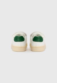 Vita sneakers med gröna hälaccenter och beige gummisulor; slät läderstruktur; rundad form; två bakre ögla för ventilation.