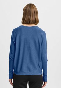 Pull en maille bleu avec un col rond et des manches longues, caractérisé par une coupe ample et une texture douce. La vue de dos montre un design minimaliste.