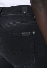 I jeans in denim nero presentano una vestibilità slim, con un'etichetta sulla tasca posteriore che recita "per tutta l'umanità" e un sottile dettaglio di cucitura.