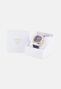 Reloj Guess con correa de silicona color navy, caja en tono dorado, esfera azul, funciones de cronógrafo, presentado en una caja de regalo blanca con la marca.