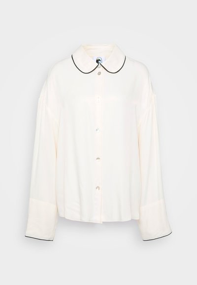 Krém színű ing puha anyagból. Lekerekített gallérral rendelkezik, fekete díszítéssel, és laza, hosszú ujjakkal van ellátva. Finom fényesség, gyöngyszerű gombokkal.