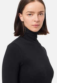 Top de cuello alto negro hecho de tela suave y elástica. Presenta un diseño ceñido y mangas largas. Estilo sencillo y minimalista.