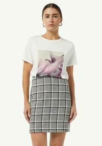 Witte t-shirt met korte mouwen en een kleurrijke grafische print; gecombineerd met een fitted zwart-wit geruite rok met een textuurweefsel.