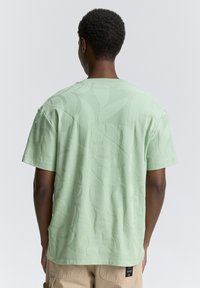 Ljusgrön t-shirt med kort ärm som har ett strukturerat bladmönster. Tyget har en mjuk finish med rundad hals och avslappnad passform.