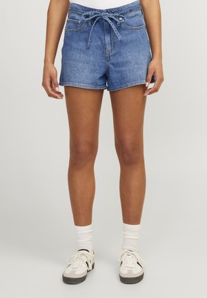 Pantalones cortos de mezclilla en azul claro con cintura ajustable, bolsillos frontales y un dobladillo ligeramente deshilachado, combinados con calcetines blancos y zapatillas.